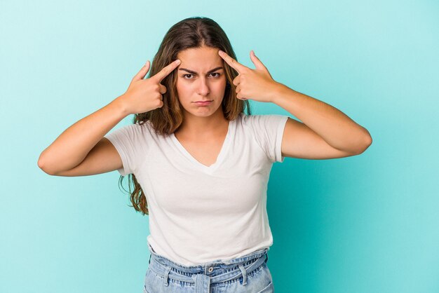 Jeune femme caucasienne isolée sur fond bleu concentrée sur une tâche, gardant les index pointant la tête.