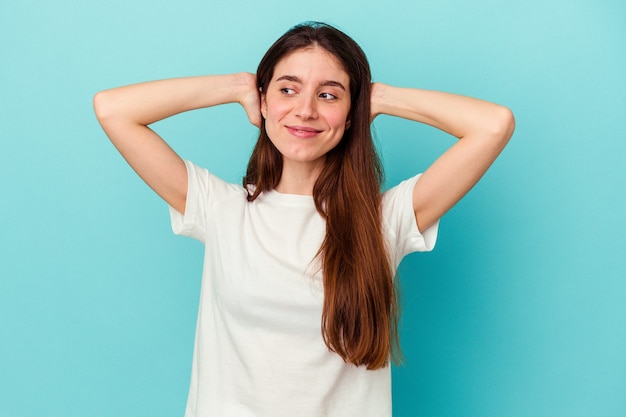 Jeune femme caucasienne isolée sur fond bleu, confiante, les mains derrière la tête.