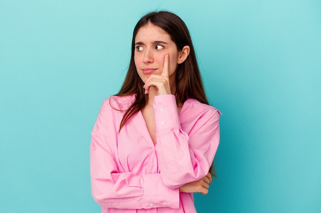 Jeune femme caucasienne isolée sur fond bleu contemplant, planifiant une stratégie, réfléchissant à la manière d'une entreprise.