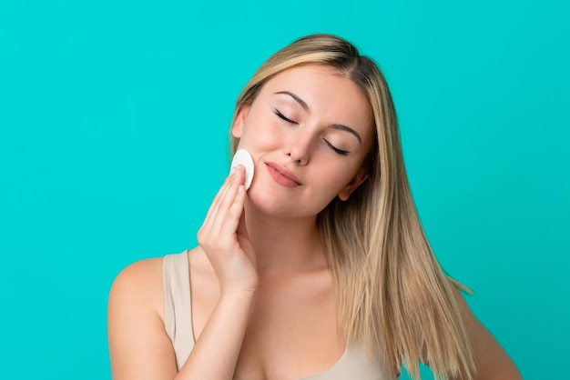 Jeune femme caucasienne isolée sur fond bleu avec un coton pour enlever le maquillage de son visage