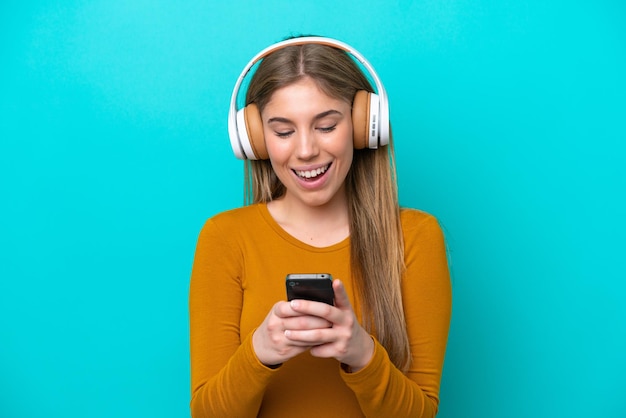 Jeune femme caucasienne isolée sur fond bleu, écouter de la musique et à la recherche de mobile