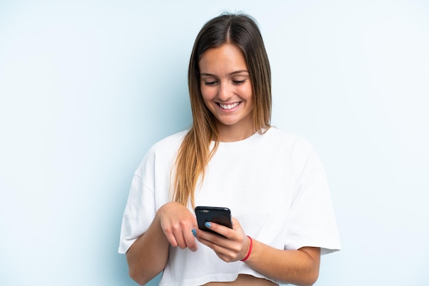 Jeune femme caucasienne isolée sur fond bleu envoyant un message ou un e-mail avec le mobile