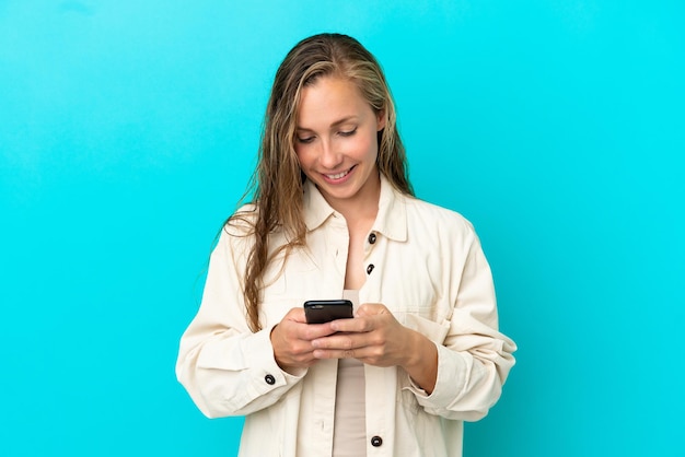 Jeune femme caucasienne isolée sur fond bleu envoyant un message avec le mobile