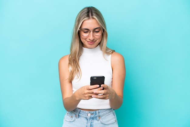 Jeune femme caucasienne isolée sur fond bleu envoyant un message avec le mobile