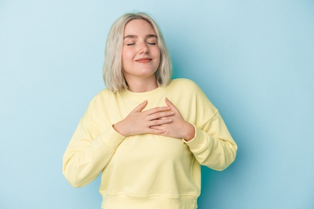 Jeune femme caucasienne isolée sur fond bleu a une expression amicale, appuyant la paume sur la poitrine. Notion d'amour.