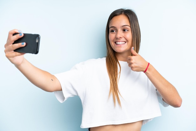 Jeune femme caucasienne isolée sur fond bleu faisant un selfie avec téléphone portable