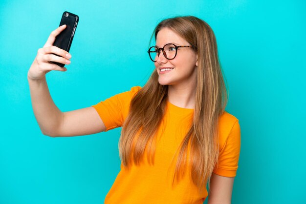 Jeune femme caucasienne isolée sur fond bleu faisant un selfie