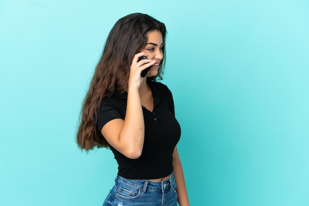 Jeune femme caucasienne isolée sur fond bleu en gardant une conversation avec le téléphone portable avec quelqu'un