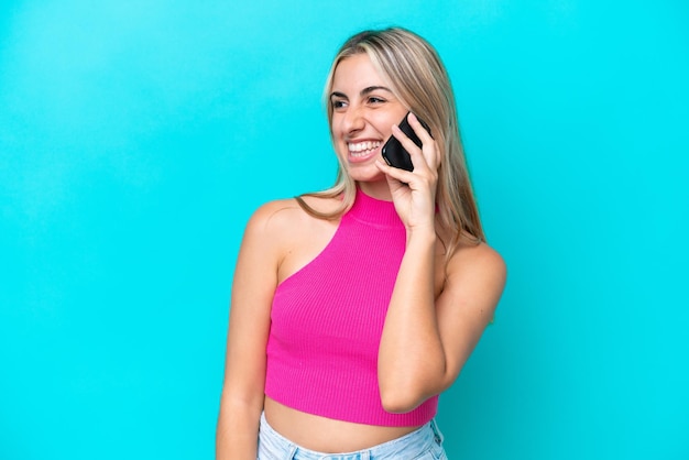 Jeune femme caucasienne isolée sur fond bleu gardant une conversation avec le téléphone portable avec quelqu'un