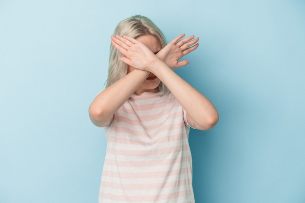 Jeune femme caucasienne isolée sur fond bleu en gardant les deux bras croisés, concept de déni.