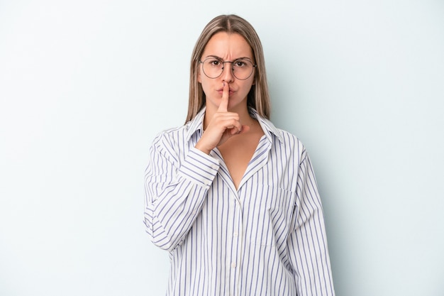 Jeune femme caucasienne isolée sur fond bleu gardant un secret ou demandant le silence.