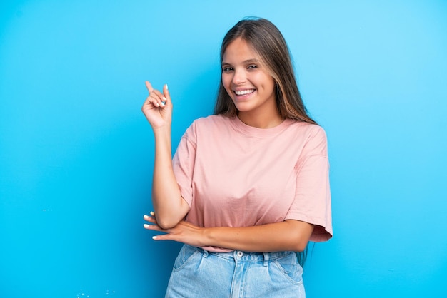 Jeune femme caucasienne isolée sur fond bleu heureux et pointant vers le haut