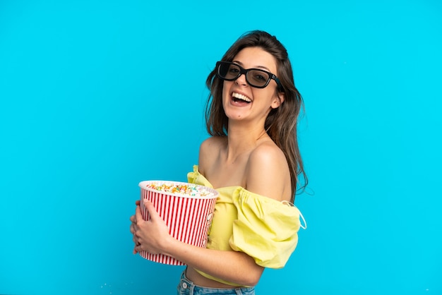 Jeune femme caucasienne isolée sur fond bleu avec des lunettes 3d et tenant un grand seau de pop-corn