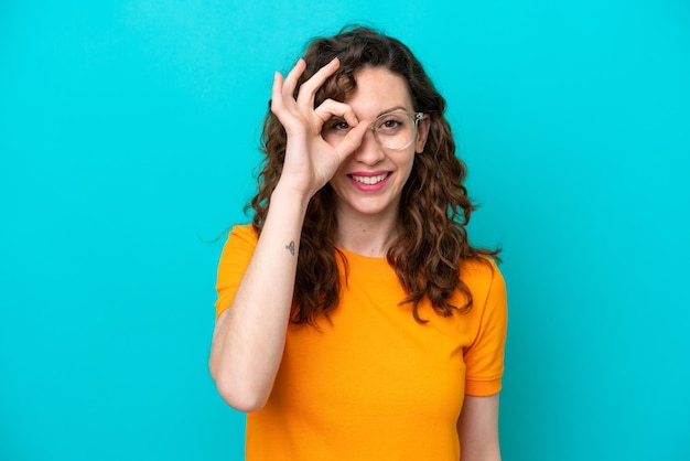 Jeune femme caucasienne isolée sur fond bleu avec des lunettes avec une expression heureuse