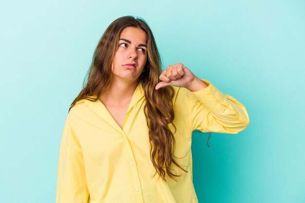 Jeune femme caucasienne isolée sur fond bleu montrant un geste d'aversion, les pouces vers le bas. Notion de désaccord.