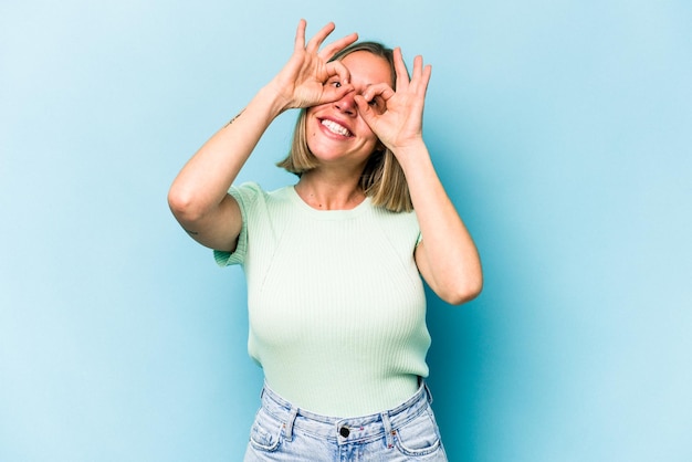 Jeune femme caucasienne isolée sur fond bleu montrant un signe correct sur les yeux