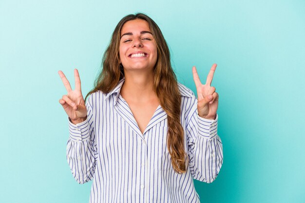 Jeune femme caucasienne isolée sur fond bleu montrant le signe de la victoire et souriant largement.