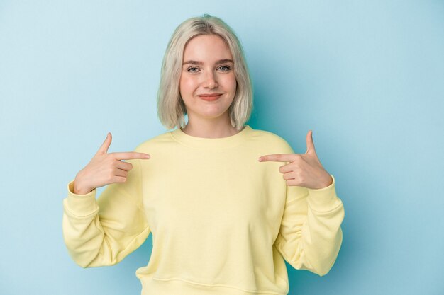 Jeune femme caucasienne isolée sur fond bleu personne pointant à la main vers un espace de copie de chemise, fière et confiante