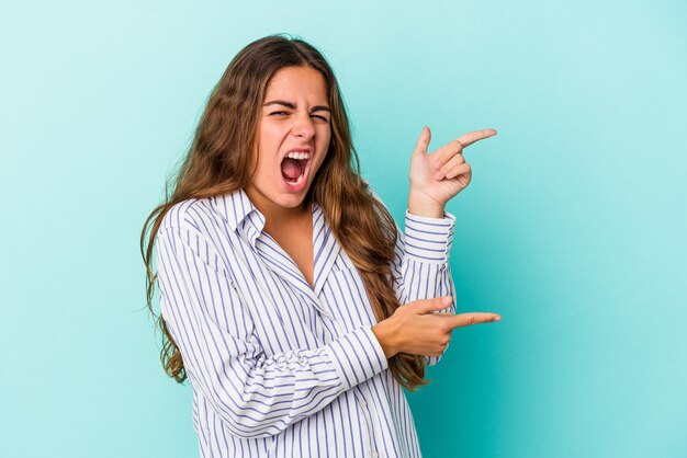 Jeune femme caucasienne isolée sur fond bleu pointant avec les index vers un espace de copie, exprimant l'excitation et le désir.