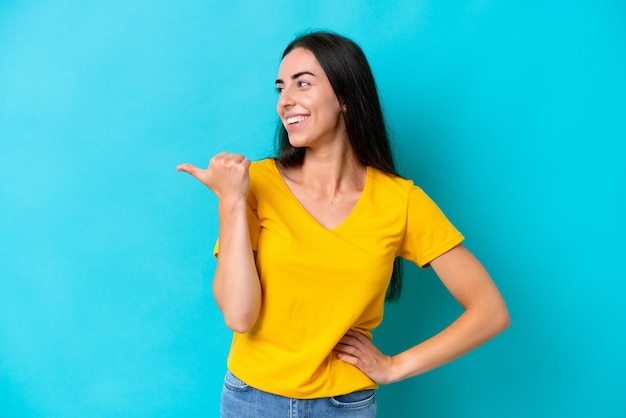 Jeune femme caucasienne isolée sur fond bleu pointant vers le côté pour présenter un produit