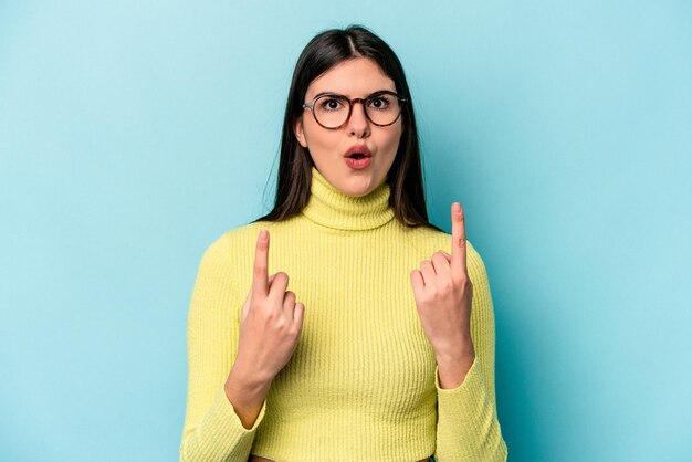 Jeune femme caucasienne isolée sur fond bleu pointant vers le haut avec la bouche ouverte