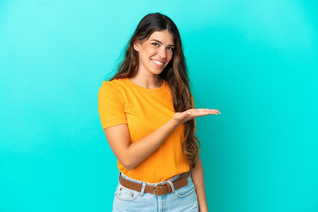 Jeune femme caucasienne isolée sur fond bleu présentant une idée tout en regardant en souriant vers