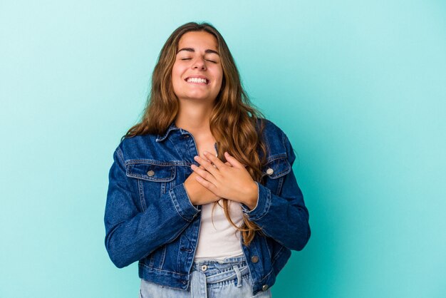 Jeune femme caucasienne isolée sur fond bleu en riant en gardant les mains sur le cœur, concept de bonheur.