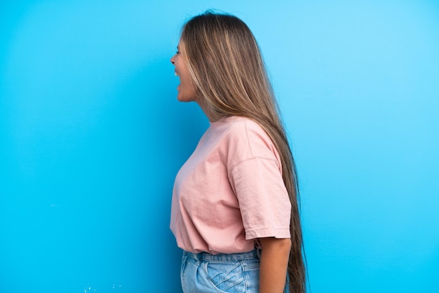 Jeune femme caucasienne isolée sur fond bleu riant en position latérale