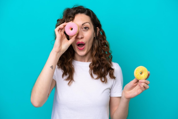 Jeune femme caucasienne isolée sur fond bleu tenant un beignet dans un œil