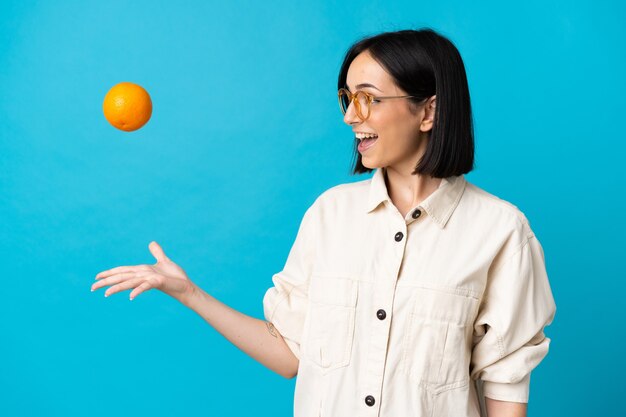 Jeune femme caucasienne isolée sur fond bleu tenant une orange