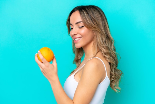 Jeune femme caucasienne isolée sur fond bleu tenant une orange