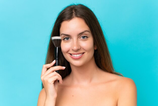 Jeune femme caucasienne isolée sur fond bleu tenant un pinceau de maquillage