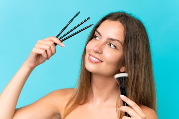 Jeune femme caucasienne isolée sur fond bleu tenant un pinceau de maquillage