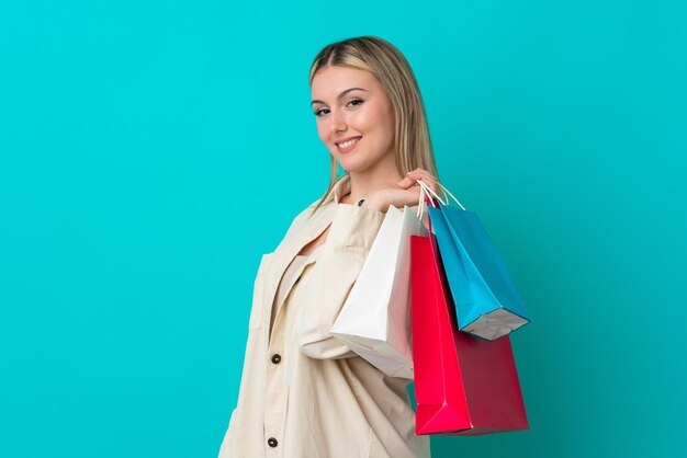 Jeune femme caucasienne isolée sur fond bleu tenant des sacs à provisions et souriant