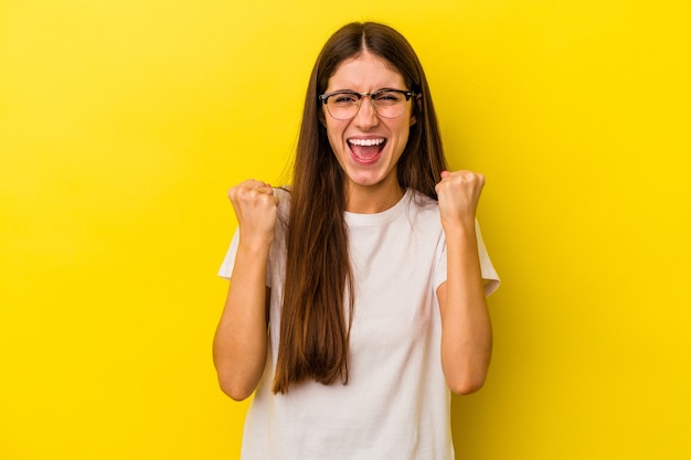 Jeune femme caucasienne isolée sur fond jaune acclamant insouciante et excitée. Notion de victoire.