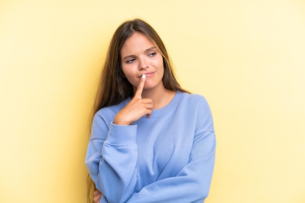 Jeune femme caucasienne isolée sur fond jaune ayant des doutes tout en levant les yeux