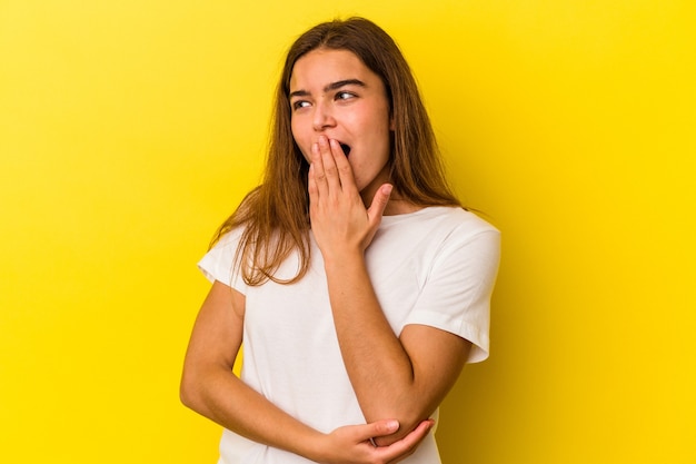 Jeune femme caucasienne isolée sur fond jaune bâillant montrant un geste fatigué couvrant la bouche avec la main.