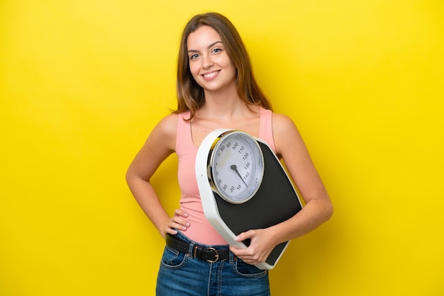 Jeune femme caucasienne isolée sur fond jaune avec balance