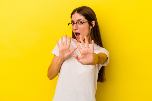 Jeune femme caucasienne isolée sur fond jaune choquée en raison d'un danger imminent