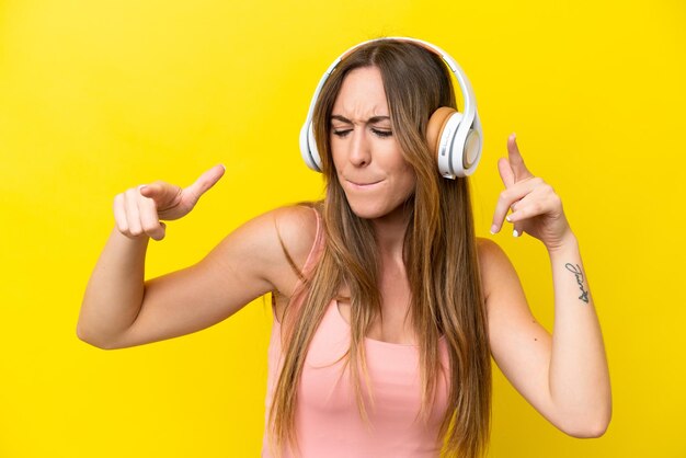 Jeune femme caucasienne isolée sur fond jaune, écoutant de la musique et dansant