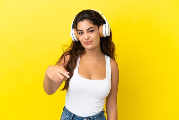 Jeune femme caucasienne isolée sur fond jaune écoutant de la musique