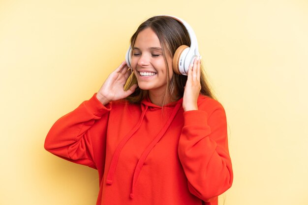 Jeune femme caucasienne isolée sur fond jaune, écouter de la musique et chanter