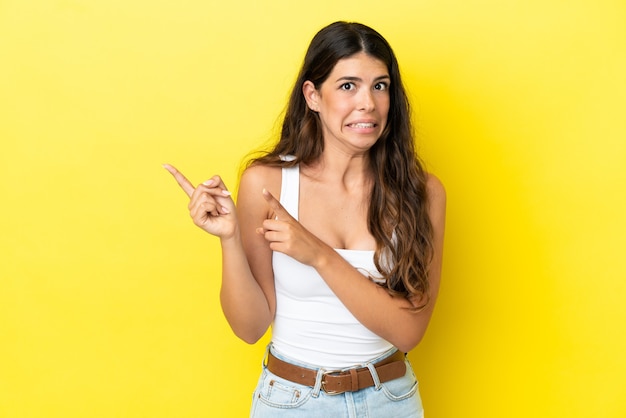 Jeune femme caucasienne isolée sur fond jaune effrayée et pointant vers le côté