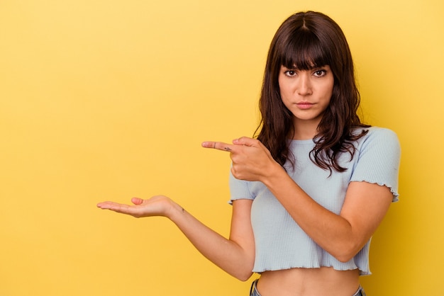 Jeune femme caucasienne isolée sur fond jaune excité tenant un espace de copie sur la paume.