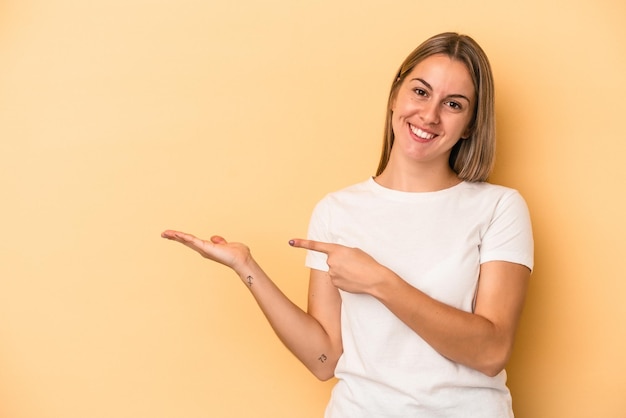 Jeune femme caucasienne isolée sur fond jaune excitée tenant un espace de copie sur la paume.