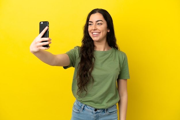 Jeune femme caucasienne isolée sur fond jaune faisant un selfie