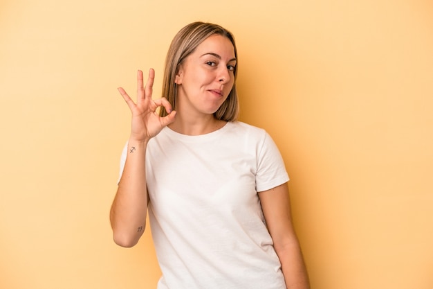 Jeune femme caucasienne isolée sur fond jaune fait un clin d'œil et tient un geste correct avec la main.