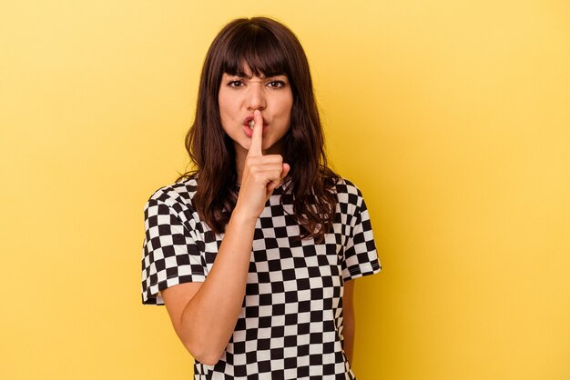 Jeune femme caucasienne isolée sur fond jaune gardant un secret ou demandant le silence.