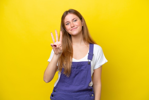 Jeune femme caucasienne isolée sur fond jaune heureux et en comptant trois avec les doigts