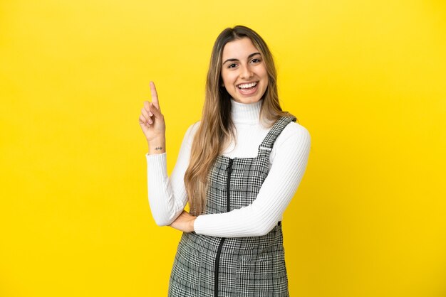 Jeune femme caucasienne isolée sur fond jaune heureux et pointant vers le haut